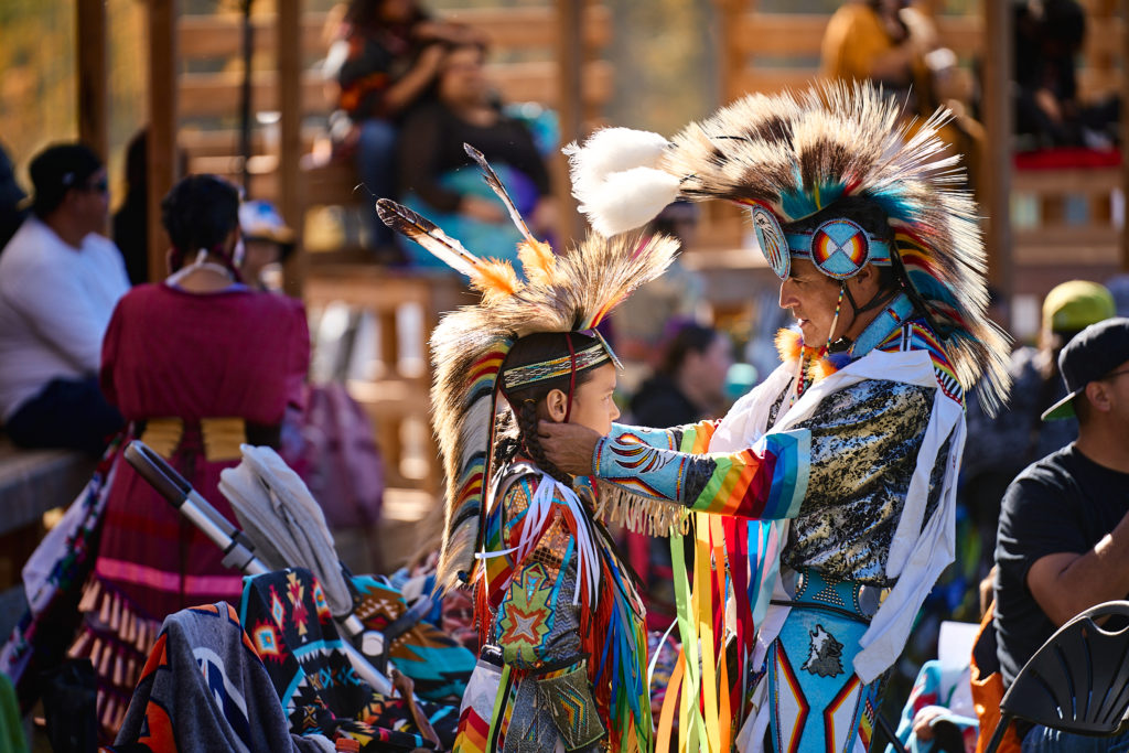 grass dancer adjusting sons regalia at pow wow